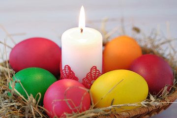 In the wicker basket lie Easter eggs and a burning candle. Close-up view.