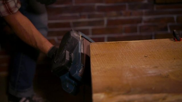 close up shot of an electric grinder that stakes ends near furniture made of wood or chipboard, a construction master works with tools in gloves