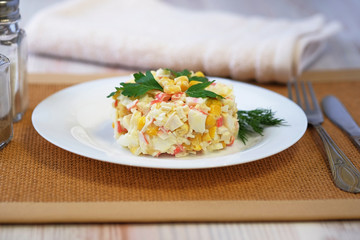 On a white plate salad of crab sticks, corn, boiled rice, eggs and with the addition of mayonnaise. The dish is decorated with leaves of green parsley. Close up view.