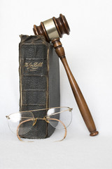 Antique leather bible with rimless eyeglasses and gavel on white background
