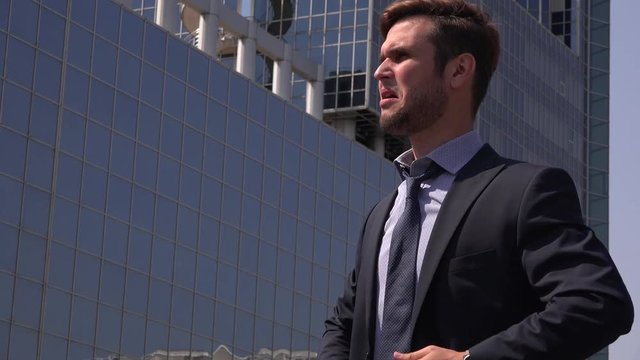 Stressed overworked business man in the city outside building loosen tie suit 4K