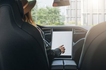 Young woman sits behind wheel in car and uses an electronic dashboard, tablet computer. Girl is...