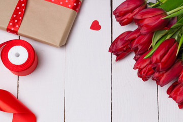 Festive spring background white wooden plaque bouquet of red tulips valentines day March 8 mother's day red hearts box with a gift red satin ribbon spring mood congratulation for a woman