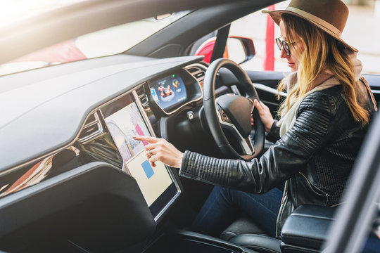 Young woman sits behind wheel in car and uses an electronic dashboard, tablet computer. Girl is traveler looking for a way through navigation system. Trip, caravanning, tourism, journey.