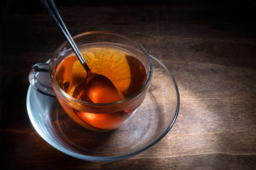 black tea freshly brewed in a glass cup and a spoon on a dark rustic wooden table, steaming hot drink against cold and flu, creative lightning, copy space