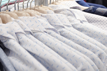 Men's shirts made of cotton light white color on the tremps in the store. Clothes sale. Photo with shallow depth of field.