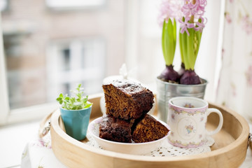 Chocolate cupcake with sugar and coffee. Breakfast on a wooden tray and flowers. View from the window to the city.
