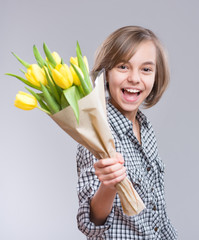 Beautiful girl with bunch of flowers on gray background. Smiling child with bouquet of yellow tulips as a gift. Happy mothers or Valentines day! 
