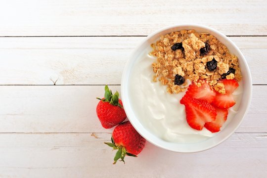 Bowl of yogurt with strawberries and granola, over a white wood background. Flat lay.