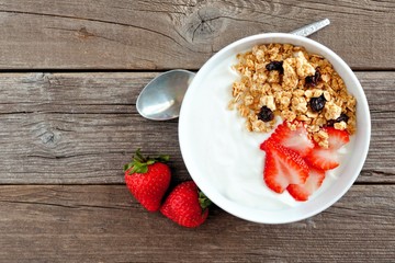 Bowl of yogurt with strawberries and granola over a rustic wood background. Flat lay.