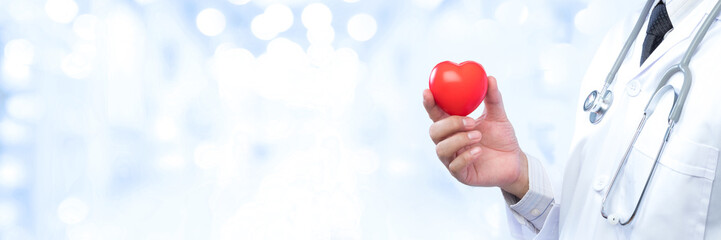 Professional medical doctor holding a red heart ball on blur office in the hospital and bokeh...