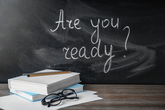 Blackboard with question "Are you ready?" and notebooks on table. Preparing for exam