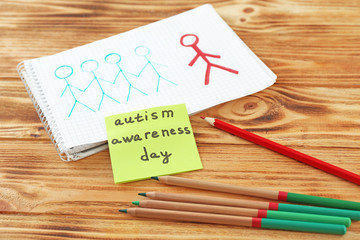 Note paper with text AUTISM AWARENESS DAY and stationery on wooden background