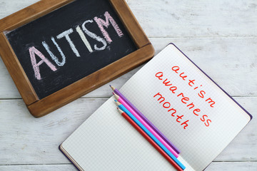 Blackboard and notepad with pencils on wooden background. Autism awareness concept