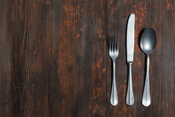 Old spoon and fork on brown wooden surface, empty space on the right, view from above