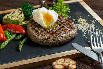 Grilled beef steak cooked on barbecue, closeup on dark wooden table background. Fresh juicy roasted red meat on black stone board, pepper and rosemary. Restaurant food, delicious dish
