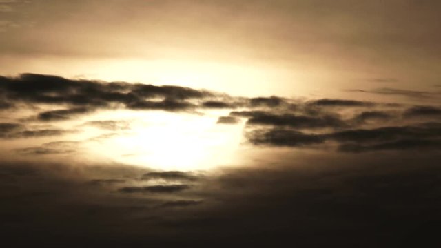 Time lapse as glowing sun drops behind dark clouds at sunset, day to night.