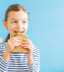 Little smiling girl eating an healthy sandwich with salad and avocados