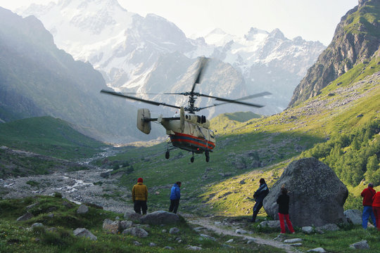 Rescue operation with helicopter in high mountains valley against the background of huge icy peaks and grassy slopes