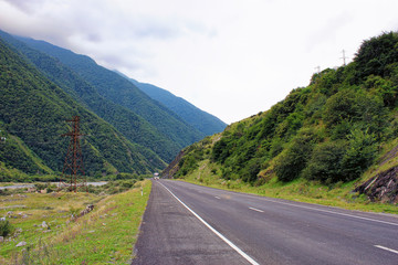 A truck is coming in the opposite direction on the highway through the mountain valley between high green ranges under cloudy sky.