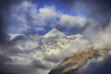 View on sunlit high icy mountain peak through the clouds.