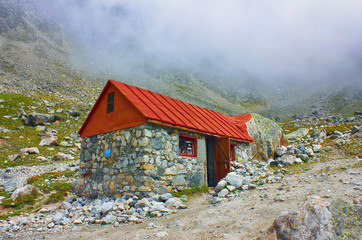 High mountains cottage for tourist and climbers rest on cloudy background.