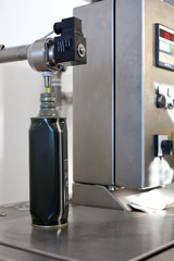 Close up of an oil dispenser in a modern oil mill, with a green aluminium bottle