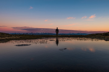 Man standing on rock facing scenic montain sunset at lake