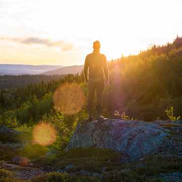 Man standing on rock facing scenic sunset with flare