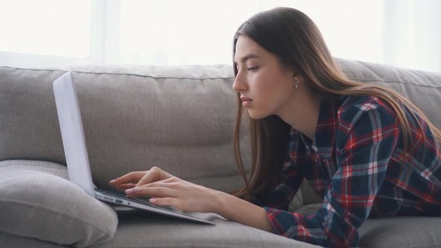 Girl lying on sofa while typing on laptop