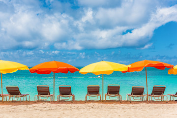 Beach chairs and umbrellas vacation background - colorful parasols lined up on sand of Sint Maarten beach, Dutch Antilles, Caribbean island. Tropical travel holiday landscape.
