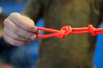 bright orange climbing rope with knots in the hands of a child in green t shirt