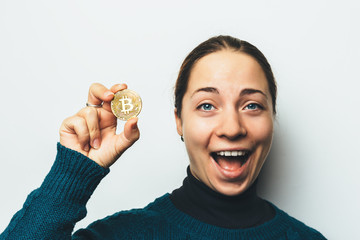 Young happy smiling girl shows Golden Bitcoin coin in hand - symbol of cryptocurrency, new virtual money