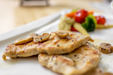 Grilled chicken steak with small mushroom and muchroom sauce in the white dish in the natural light in restaurant.