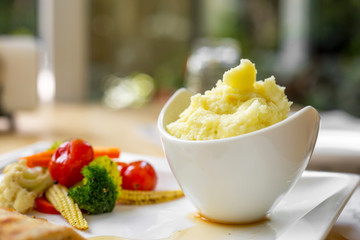 Grilled chicken steak with small mushroom and muchroom sauce in the white dish with baked potato in the natural light of restaurant.