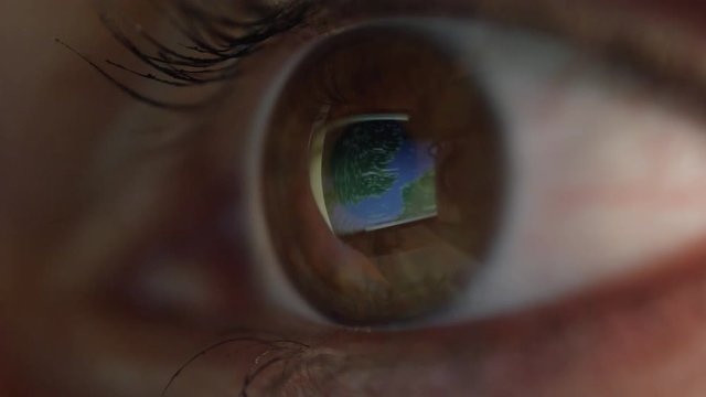 MACRO CLOSE UP: Blinking eye looking at world map. Computer screen image, seen in a reflection on the eyeball surface, zooming into London. Tourist planning upcoming vacation in the United Kingdom.