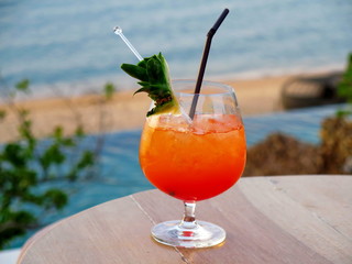 Tropical fruit cocktail on wood table and blurry pool, beach, tree and blue sea background, Hello summer welcome April with cool delicious drink