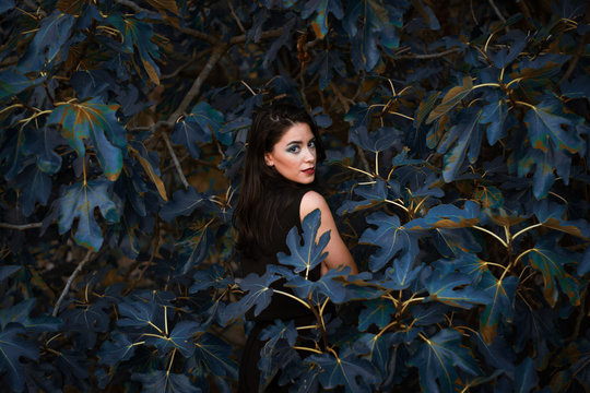a Caucasian model poses, surrounded by blue leaves and looks at you taking you into her magical world
