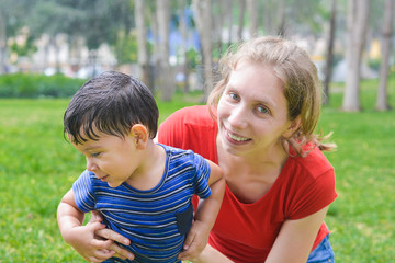 Happy biracial family in the summer park - caucasian mother with her little latin boy. 