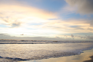 view of the blue sky and full of morning clouds on a beach with sea water reaching in the sand.