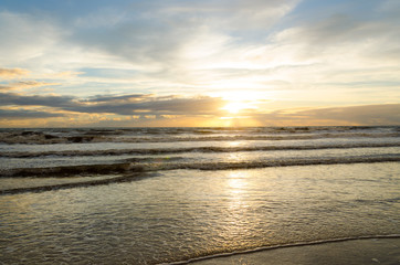 view of sunrise on a beach with the reflection of the sun in the sea water.