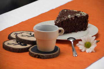 Chocolate cake slice with white chocoalte cream in plate with cup of coffee