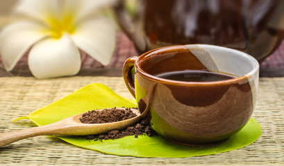 Coffee lover.Coffee cup on green leaf with roasted coffee on wooden spoon.Background is a white plumeria and coffee pot.