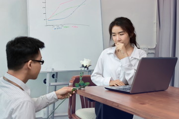 Fototapeta premium Vintage toned image of surprised young Asian business woman receiving a white roses on Valentine's day in office. Affectionate couple in love concept.
