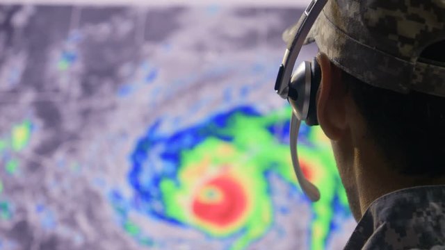 Man in military fatigues monitoring hurricane activity on screen