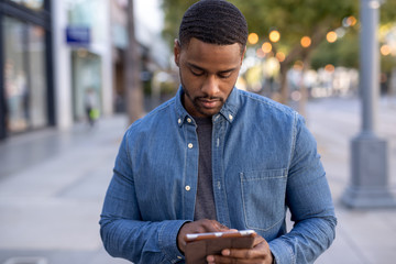 Young black man using tablet computer walking