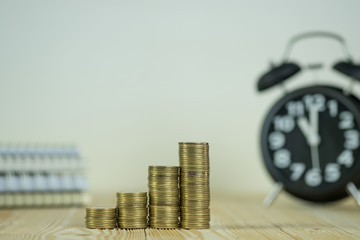 Steps of coins stack with vintage alarm clock and pen, notebook paper on wooden working table with copy space for text, financial and business planning concept..
