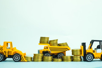Mini forklift bulldozer truck and road roller machine with pile of gold coin, with copy space, business finance and banking industrial concept.