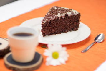 Fototapeta na wymiar Chocolate cake slice with white chocoalte cream in plate with cup of coffee