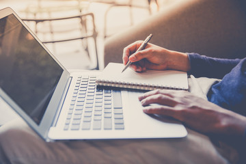 Business man working on laptop computer and writing notebook in late afternoon, close up, vintage style.